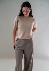 Beige gebreide trui met korte mouwen, gecombineerd met lichtgrijze geplooide broeken, wat zorgt voor een ontspannen en gecoördineerde outfit.