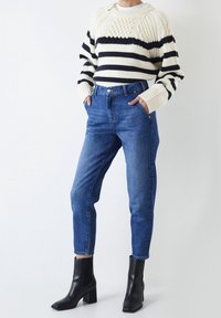 Maglione a righe in crema e blu navy, abbinato a jeans a vita alta blu e stivali neri alla caviglia con punta quadrata e tacco largo.
