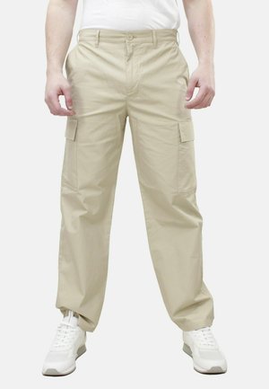 Pantaloni cargo beige con tasche laterali, design a gamba dritta e chiusura con bottone in vita, abbinati a sneakers bianche.