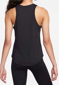 Žena v černém bezrukávovém sportovním tílku a černých legínách, zobrazená zezadu na bílém pozadí.