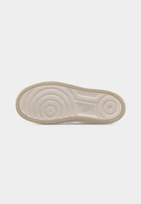 Πάτος μπεζ παπουτσιού Nike με συγκεντρικά κυκλικά σχέδια πέλματος και μικρό λογότυπο Nike Air κοντά στην καμάρα, σε απλό λευκό φόντο.