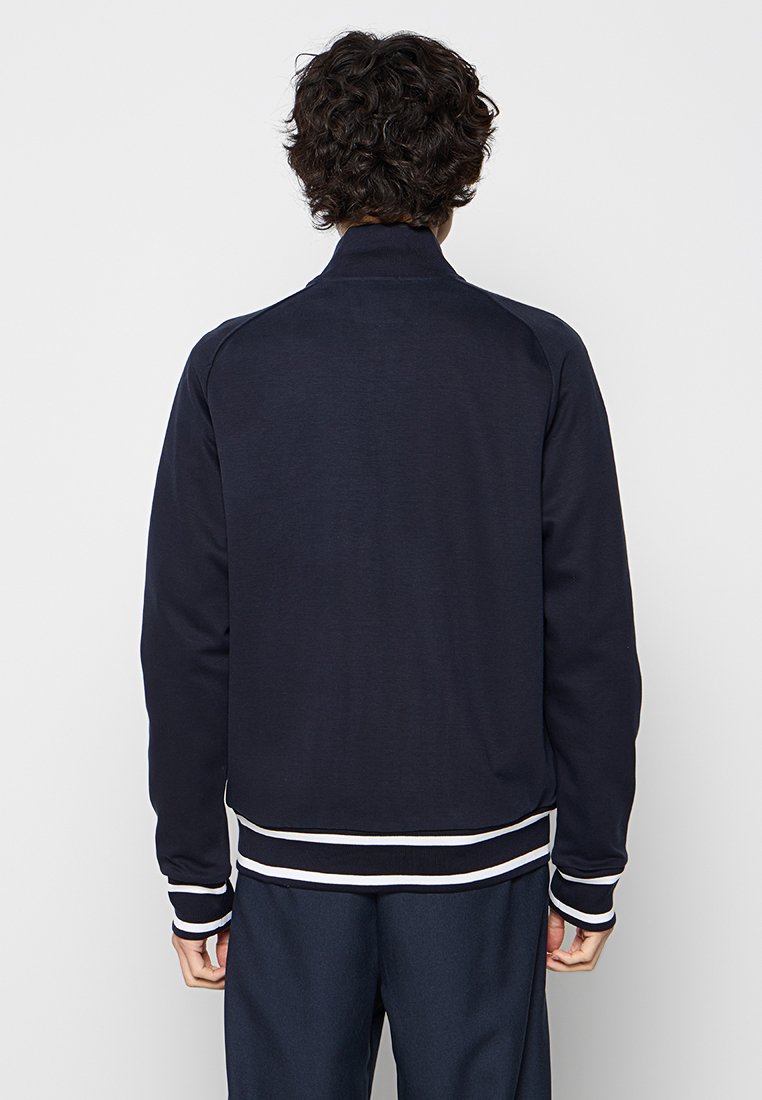 Granatowy sweatshirt z wysokim kołnierzem, z kontrastującymi białymi poziomymi paskami przy mankietach i u dołu, wykonany z miękkiej tkaniny. Gładka, wykończona powierzchnia.