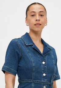 Φόρεμα από τζιν σε σκούρο μπλε χρώμα με γιακά, κοντά μανίκια, κουμπιά μπροστά και τσάκιση στη μέση. Ορατές ραφές διακοσμούν.