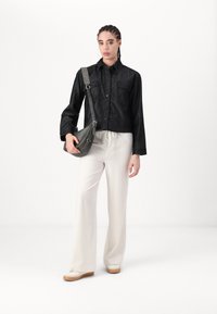 Chaqueta de mezclilla negra con un diseño de cuello y dos bolsillos en el pecho, combinada con pantalones de pierna ancha en un tono crema claro y un bolso cruzado gris.
