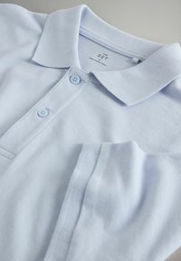 Svetlomodra bombažna polo majica z ovratnikom in dvema gumboma, položena ravno, prikazuje zložene rokave in notranjo znamko.