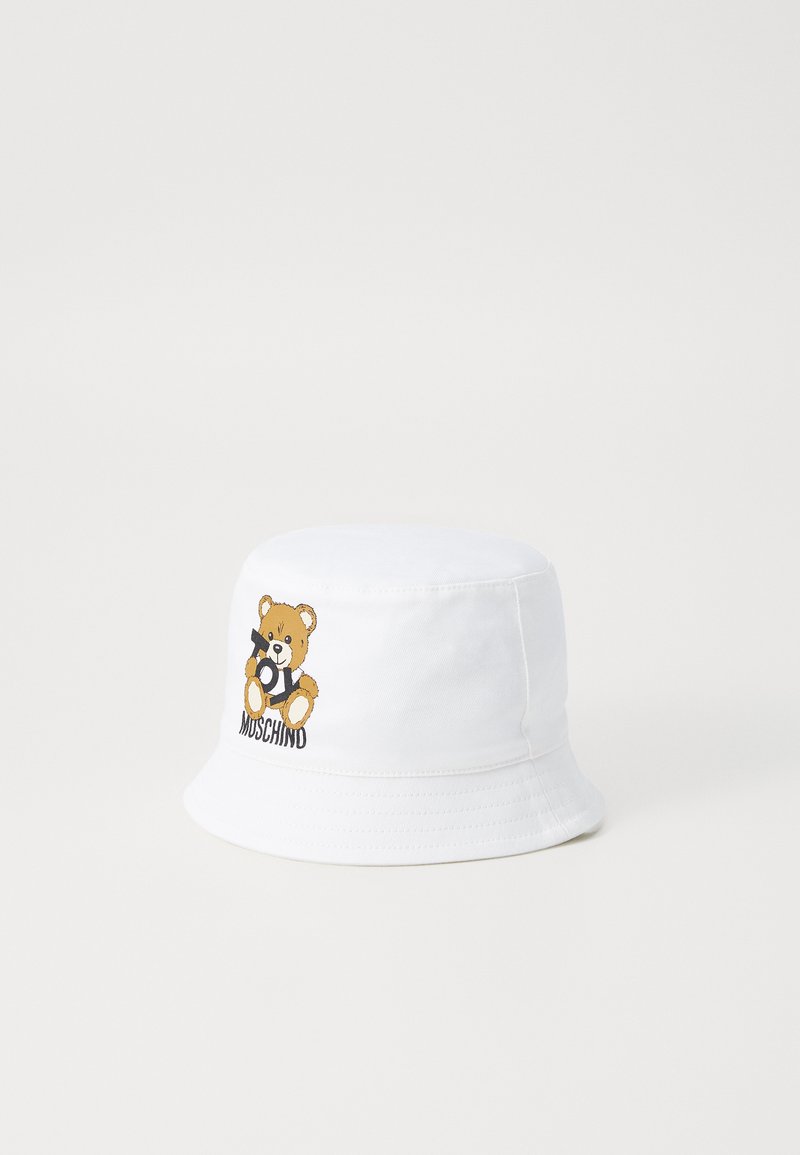 Bela bombažna klobukasta kapa z vezenim motivom medvedka, ki drži igračo. Opremljena z besedilom "MUSCHIND" pod medvedkom.