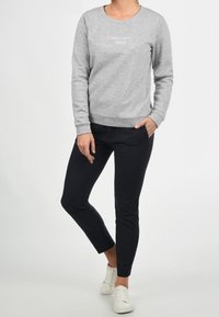 Sudadera de algodón gris con cuello redondo y puños acanalados, con texto en blanco "LAS CHICAS MUERDEN DE VUELTA". Combinada con pantalones negros de corte ajustado y zapatillas blancas.