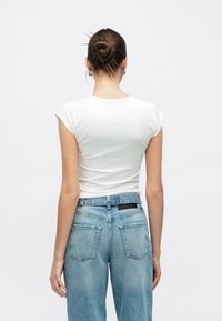 Λευκό μπλουζάκι με κοντά μανίκια σε συνδυασμό με ανοιχτό μπλε, ψηλόμεσο τζιν με μαύρη ετικέτα και δύο πίσω τσέπες. Ομαλή υφή υφάσματος.