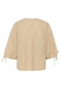 Beige blouse with diamond cut-out patterns, balloon sleeves, and tie accents at the cuffs. Soft texture with a relaxed fit.
