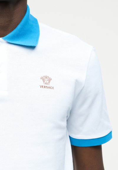 Λευκό πόλο μπλουζάκι με γαλάζιο γιακά και περιθώριο στα μανίκια, με μικρό μπρούτζινο λογότυπο Medusa της Versace στο στήθος.