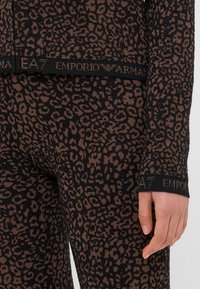 Termo súprava s leopardím vzorom v hnedej a čiernej farbe, vyrobená z textúrovaného elastického materiálu. Obsahuje pás s logom a priliehavé manžety.