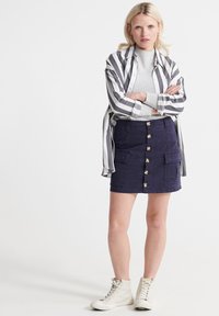 Mørkeblå denimnederdel med frontknapper og sidelommer, parret med en grå ribbestrikket sweater og en stribet sort-hvid T-shirt, afsluttet med hvide sneakers.