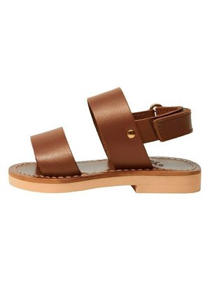 Brązowa skórzana płaska sandałka z dwoma szerokimi paskami, paskiem wokół kostki z złotą sprzączką oraz jasnobrązową podeszwą ze szwem na krawędziach.
