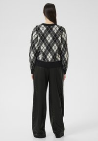 Pull en argyle noir et blanc avec un col rond et des poignets côtelés, associé à un pantalon large noir avec un motif texturé.