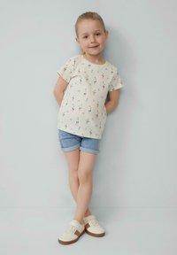 Lichtgekleurde geribde t-shirt met een bloemenpatroon, gecombineerd met denim shorts en crèmekleurige sneakers. Eenvoudig ontwerp, korte mouwen, losse pasvorm.