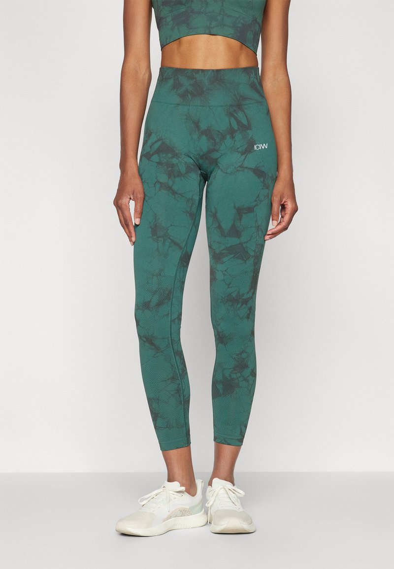 Leggings cu imprimeu de marmură verde, cu talie înaltă, realizate dintr-un material elastic, asortate cu pantofi sport albi.