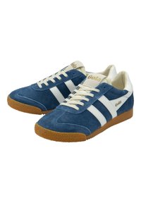 Blue suede sneakers with white stripes and a textured gum sole. Laces are light-colored; branding in gold on the tongue and side.