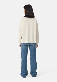 Pull crème avec une coupe décontractée texturée, associé à un jean flair bleu clair. La tenue présente des manches relaxées et des détails minimes.
