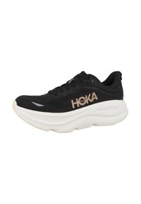 Svarte joggesko med mesh-overdel, fremtredende HOKA-logo i roségull, tykk hvit mellomsåle og teksturert gummisåle.