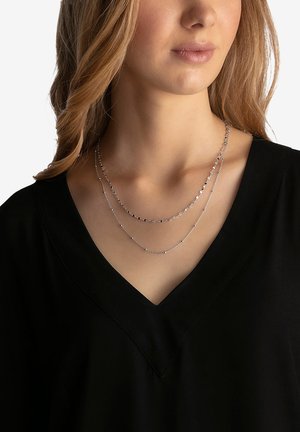 Collana a strati in argento con perle rotonde e ovali su catene sottili, indossata su una maglia nera con scollatura a V, che evidenzia il suo design delicato.