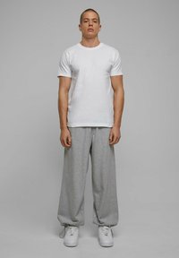 Hvid T-shirt med rund hals, grå vid ben sweatpants og hvide sneakers. Simpelt, afslappet design med en glat tekstur. Ingen bemærkelsesværdige mønstre.