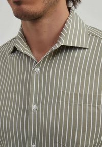 Chemise verte à rayures blanches verticales, dotée d'un devant à boutons, d'un col et d'une poche poitrine. Tissu texturé.