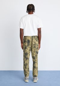Camouflage-mønstrede bukser i nuancer af grøn og beige, med en løs pasform og elastisk talje, parret med en ensfarvet hvid t-shirt.