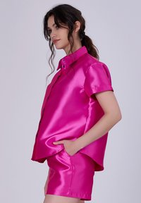 Chemise courte en satin fuchsia à manches courtes avec un col pointu, fermeture à boutons sur le devant et coupe décontractée, associée à un short en satin assorti.