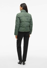Grøn quilted puffer-jakke med høj krave, der har et cropped design og syede paneler. Båret med sorte lige ben jeans og hæle støvler.