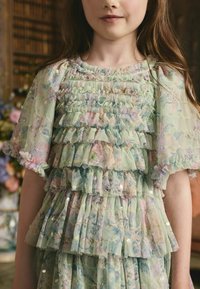 Világoszöld ruha réteges, fodros anyagból, pasztellszínű virágmintákkal. Rövid ujjú, apró flitterekkel díszítve.