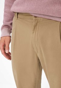 Beige katoenen broek met een gladde textuur en een rechte snit, voorzien van een enkele voorkantzak en eenvoudige stikdetails.