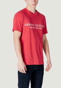 T-shirt in cotone rosso con la scritta "ARMANI EXCHANGE MILANO/NEW YORK" stampata in bianco sul davanti, collo a giro e maniche corte.