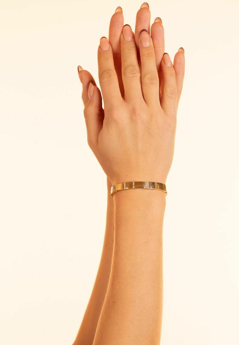 Guldmetallarmband med växlande platta och texturerade segment. Slät yta med en enkel, elegant design.