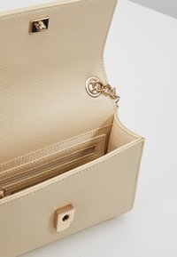Beige textured handbag with a magnetic clasp, gold hardware, and an interior zipper pocket. Smooth, structured design with minimal detailing.
