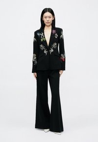 Fekete blézer színes virágos hímzéssel, fekete, szárában bővülő nadrággal párosítva. Sima anyag, strukturált reverek, és látható patentok nélkül.