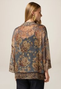 Kimono floreale trasparente in blu con motivi di rose pesca e marrone. Presenta maniche larghe e un bordo decorato all'orlo.