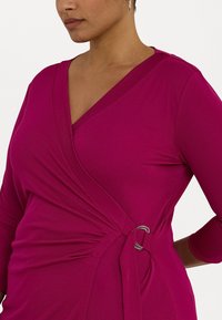 Fuchsia omslagskjole med trekvart ermer, dyp V-hals og en metallringdetalj i midjen med rynkedesign på siden.