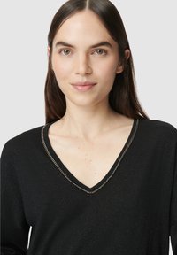 Schwarzer V-Ausschnitt-Pullover mit strukturiertem Finish und silberner Kettenakzent entlang des Ausschnitts. Enganliegendes Design mit langen Ärmeln.