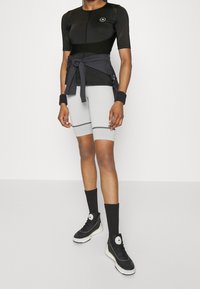 Musta lyhythihainen paita, jossa on hengittäviä yksityiskohtia, harmaat puristusshortsit, mustat polveen ulottuvat sukat ja mustat lenkkarit, joissa on valkoinen pohja.