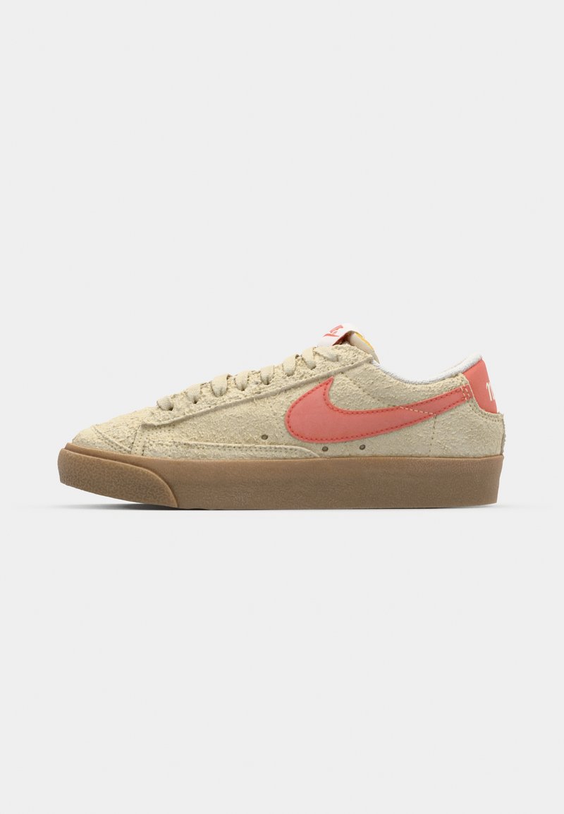 Des baskets Nike avec une tige en daim beige, un swoosh rose, une semelle en caoutchouc et des détails texturés sur le bout et les côtés.