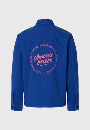 Μπλε σακάκι με μακριά μανίκια και κόκκινο κυκλικό κείμενο στην πλάτη που γράφει «Amour Hotels» και περιλαμβάνει τοποθεσίες όπως το Παρίσι και τη Νίκαια.