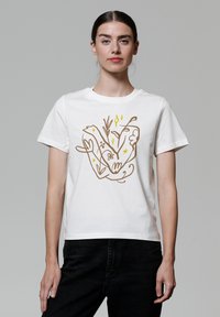 T-shirt en coton blanc avec un design illustré de mains et de plantes en brun et jaune, de coupe décontractée et à manches courtes.