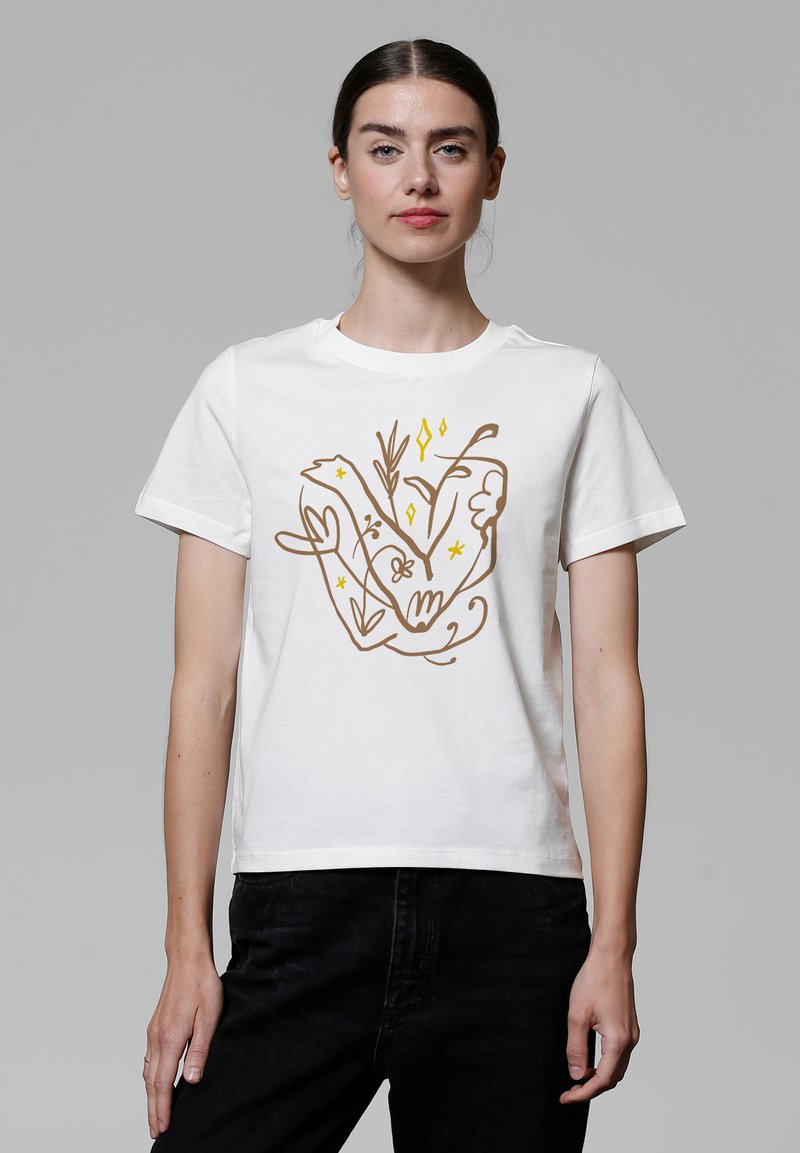 T-shirt en coton blanc avec un design illustré de mains et de plantes en brun et jaune, de coupe décontractée et à manches courtes.