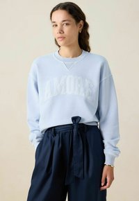 Lichtblauwe sweatshirt met "AMORE" in verhoogde letters, gecombineerd met donkerblauwe broeken met een gestrikt taille. Zachte stof, ontspannen pasvorm.