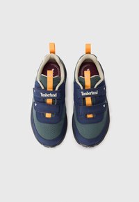 Et par marinblå og grønne Timberland barnesko med oransje drahåndtak og doble borrelåser på hvit bakgrunn.