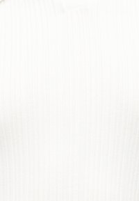 Λευκός ριμπ πλεκτός πουλόβερ με V λαιμόκοψη και λεπτομέρειες στη ραφή του αριστερού ώμου σε λευκό φόντο.