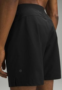Svarta idrottsshorts med en slät yta, elastisk midja och en sidoklyvning. Har en liten logotyp på nedre vänstra benet.