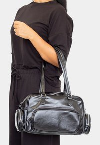 Bolso de mano de cuero negro con dos asas para el hombro, que cuenta con un compartimento principal con cremallera, un bolsillo frontal y un bolsillo lateral con cremallera para almacenamiento.