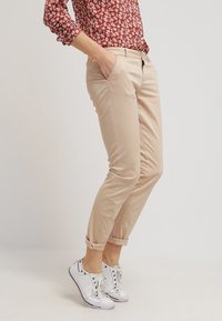 Beige chinos med en slim fit og oprullede cuffs, lavet af letvægtsstof. Kombineret med hvide sneakers, båret afslappet af en person.