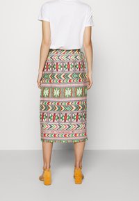 Patterned midi skirt in multicolor with geometric designs; fabric appears smooth. Paired with a white t-shirt and yellow block-heel sandals.